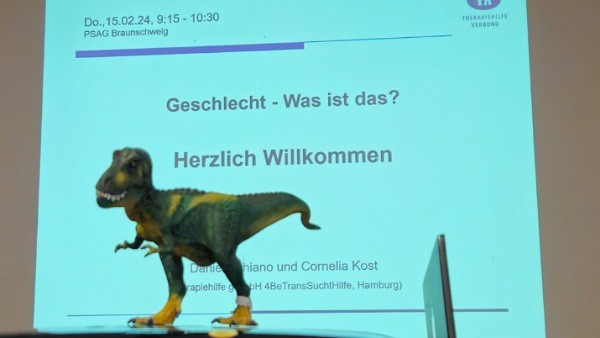 Präsentation an Leinwand mit T-Rex Figur im Vordergrund und dem Text:
PSAG Braunschweig
Geschlecht - Was ist das?
Herzlich Willkommen
Daniel Schiano und Comelia Kost
