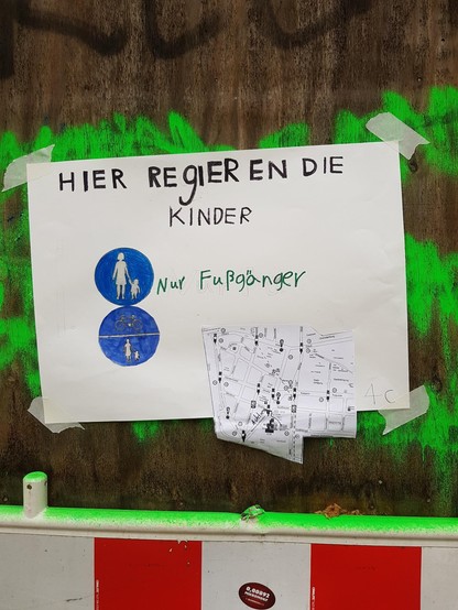 Ein von Kindern gestaltetes Demo Plakat mit der Aufschrift
Hier regieren die Kinder
und zwei gemalten Schildern, für Fußweg und Fuß/Radweg zusammen