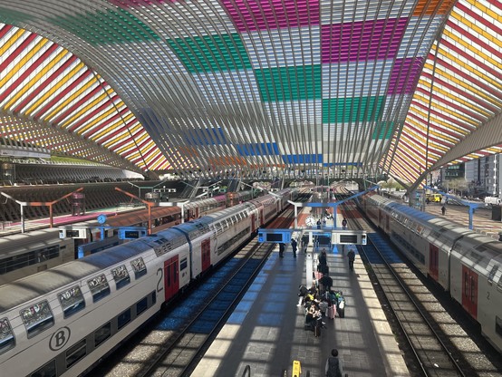 Picture from the overpass at Liège Guillemins station. 2 SNCB double deck trains in the platforms either side. Colourful huge high roof above. 
