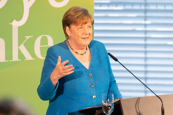 Auf dem Bild zu sehen ist die Bundeskanzlerin a.D. Angela Merkel. Sie hält eine Rede vor grünem Hintergrund.