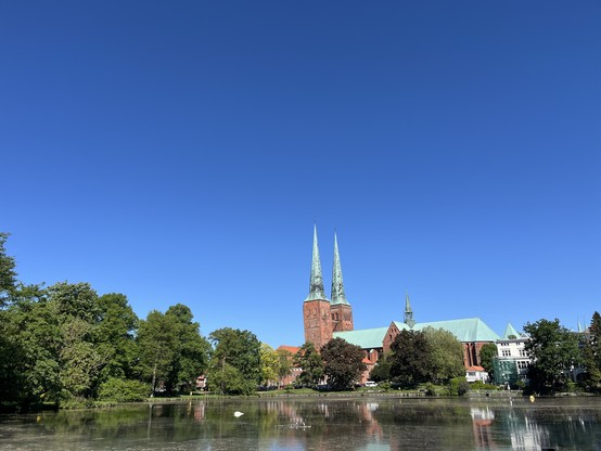 Lübeck cathedral in the centre. Trees to left. Pond in front. Blue sky above 