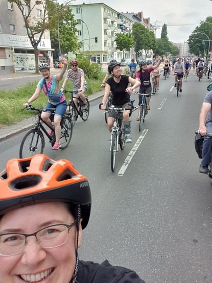 Selfie beim Rad fahren, Corinna mit Helm im Vordergrund,  dahinter fröhliche Menschen mit dem Rad, die Anwohnenden zu winken