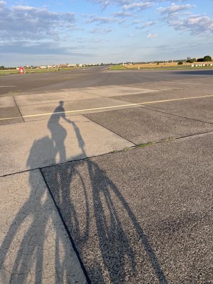 A long shadow of a bike on an expanse of an old concrete runway 