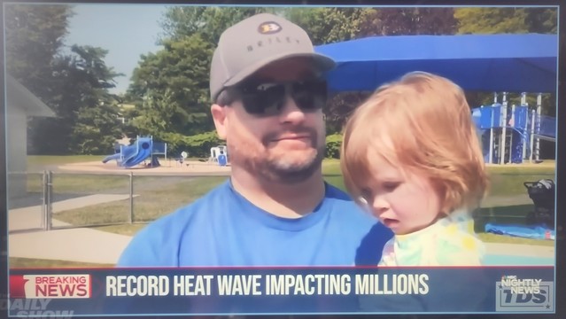 Ein amerikanischer Fernsehsender berichtet über eine Rekordhitzewelle. In einem Interview ist ein Vater zu sehen, der Cappy und Sonnenbrille trägt. Das kleine Kind auf seinem Arm hat keinerlei Sonnenschutz.