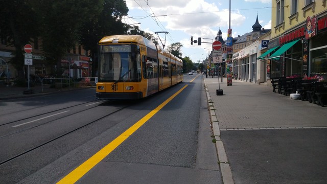 Ein frischer, gelber Strich auf der Straße markiert einen Radweg. Links davon eine gelbe Straßenbahn. Beschilderung: Einbahnstraße, Fahrrad frei.