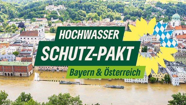 Plakat mit der Aufschrift 

Hochwasser Schutz-Pakt
Bayern & Österreich 

Im Hintergrund sieht man eine überflutete Stadt.