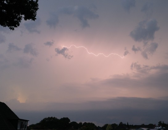 Dunkler Himmel. In der Bildmitte ein horizontaler Blitz zwischen zwei kleinen Wolken.